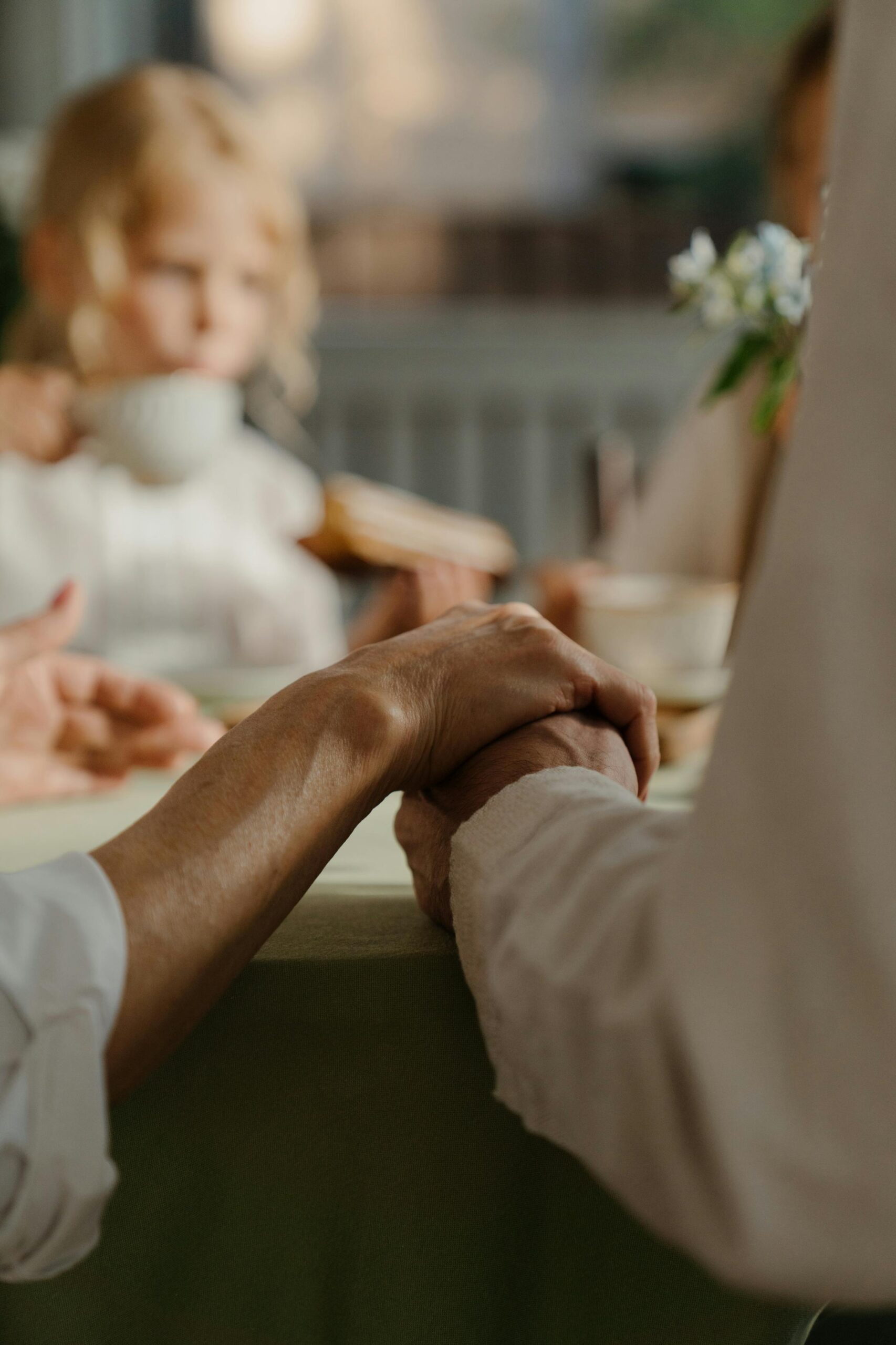 Elderly couple holding hands during a cozy family gathering indoors.